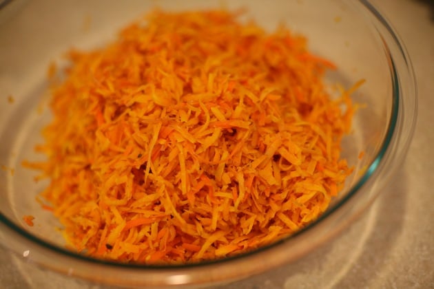 Adding blanched shredded carrots into a bowl. 