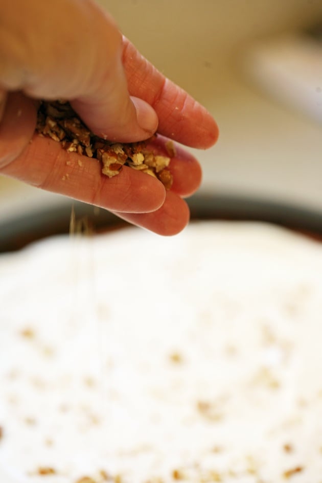 Sprinkling crushed pecans on the cake.