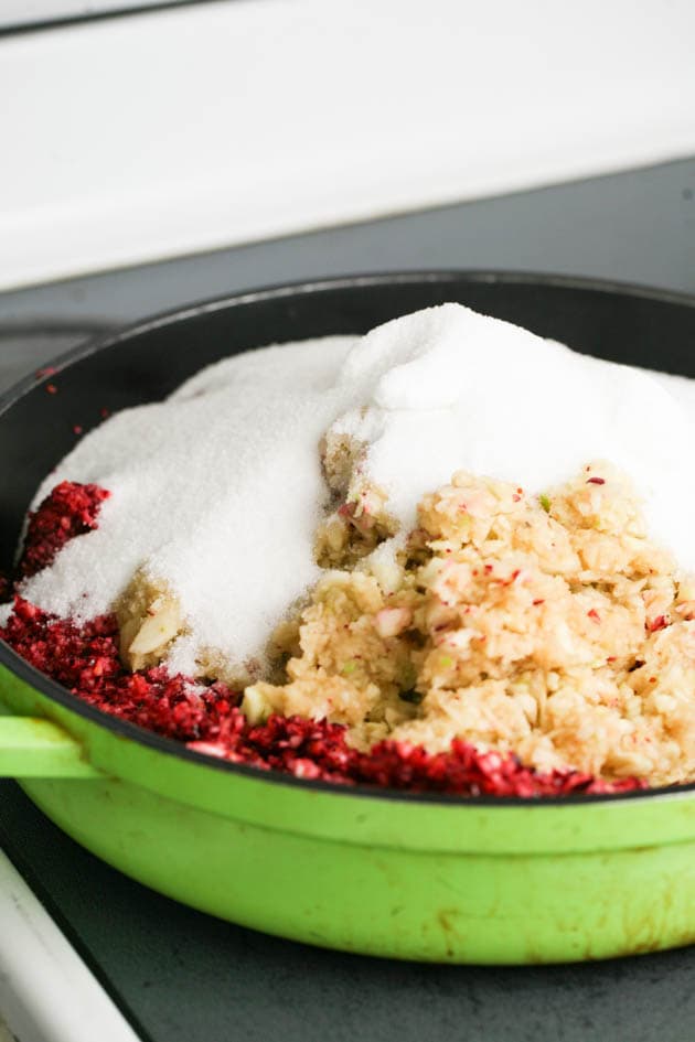 Adding cranberries, apples, and sugar to a shallow pot. 