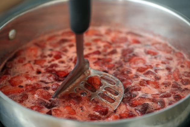 mashing the strawberries with a potato masher