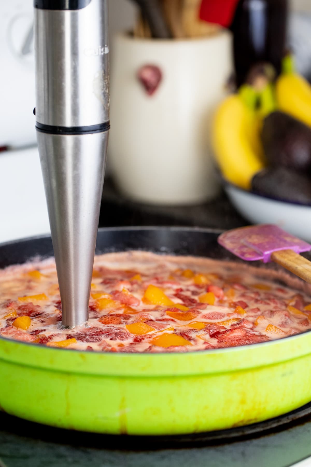 mashing the fruit with an immersion blender
