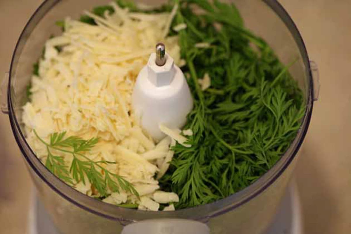 adding parmesan and carrot tops to the food processor